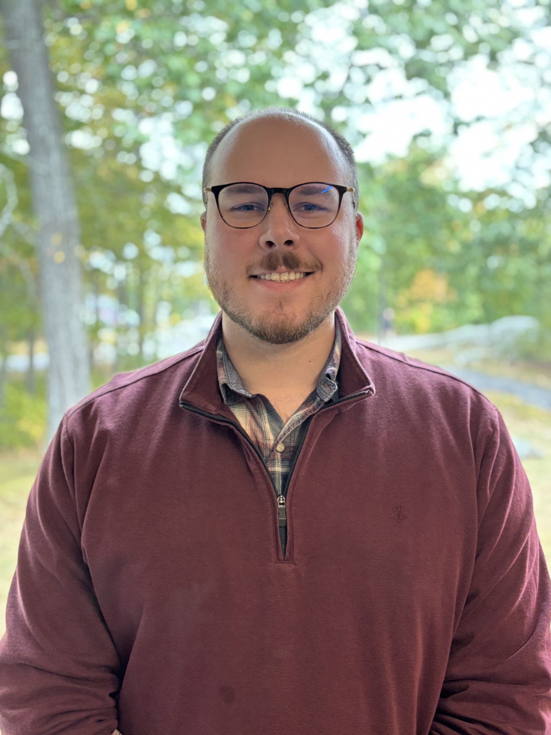 smiling man wearing glasses with trees in background